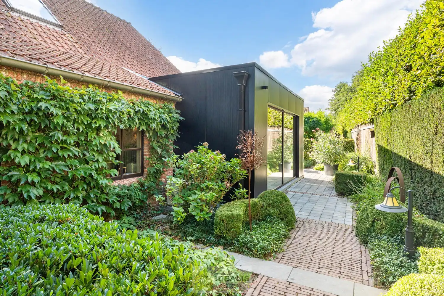 IDYLLISCH GELEGEN BIJZONDERE EIGENDOM BESTAANDE UIT RIANT WOONHUIS, APART BEWOONBAAR BIJGEBOUW EN ATELIER OMGEVEN DOOR EEN SCHITTERD AANGELEGDE TUIN EN WEILAND. Het domein is toegankelijk zowel aan de mooie Urnenveldstraat doch ook via een uitzonderlijk mooie oprijlaan toegankelijk langs de boszijde van het perceel. Deze vrijstaande woning, gebouwd in 1986, beschikt over een sfeervolle leefruimte in vol contact met de tuin en biedt een heerlijke atmosfeer dankzij de centraal geplaatste speksteenkachel. Op de verdieping beschikt de woning over slaapkamers en sanitair. Een absolute meerwaarde is het afzonderlijk volledig ingericht bijhuisje, centraal op het perceel, voorzien van alle woonfaciliteiten. Verder is er de mogelijkheid om wonen/werken te combineren via het knap afgewerkte atelier, met vergezicht op het eigen weiland. Geschikt voor kandidaten op zoek naar een ruime en instapklare parel met een idyllische uitstraling! foto 4