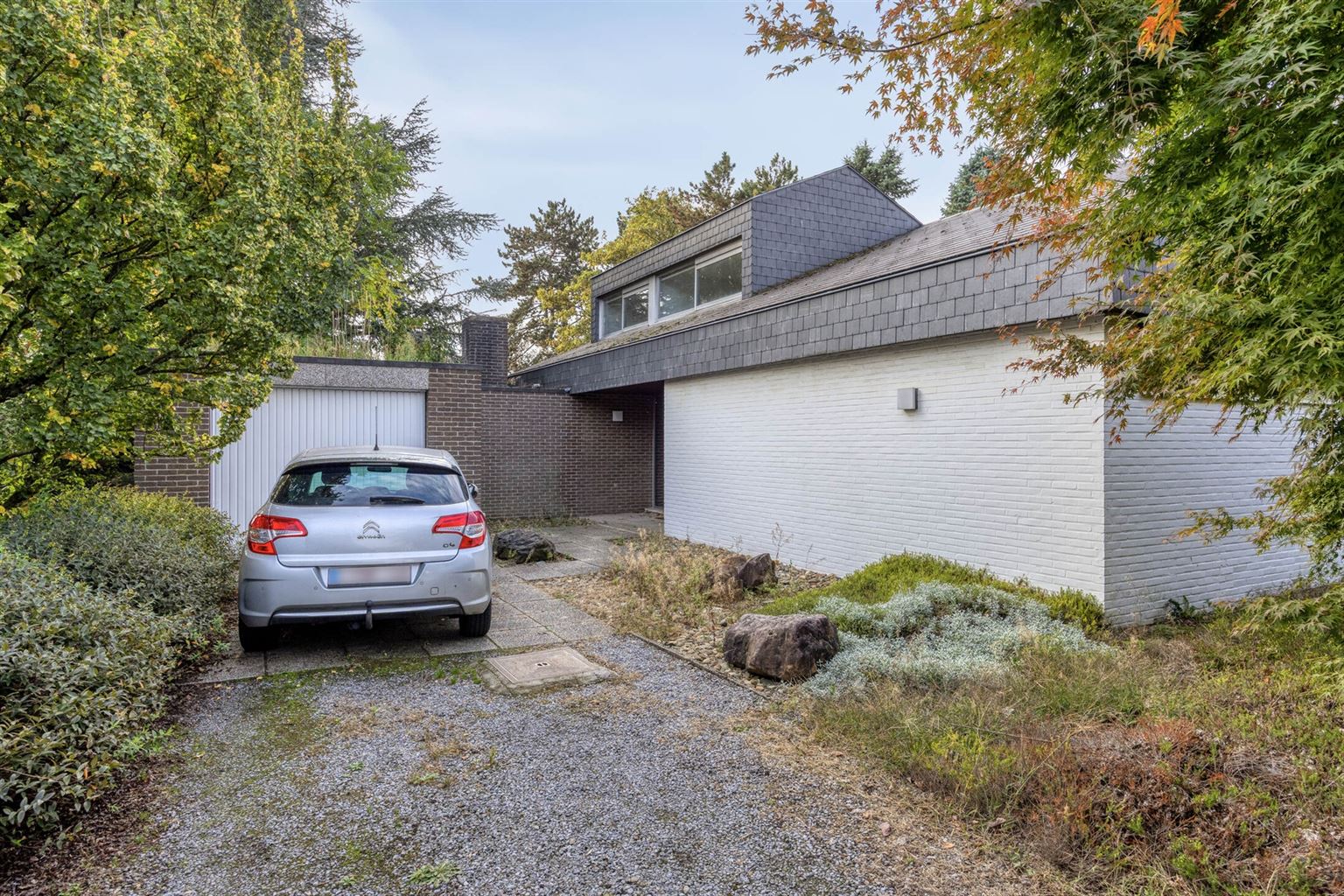 Hoofdfoto van de publicatie: Vrijstaande woning in 70s stijl op een uniek perceel van 15a93ca met 5 slaapkamers, inpandige garage en riante tuin, gelegen op een rustige toplocatie nabij het centrum van Maaseik.